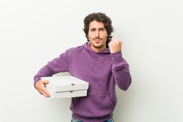 Jonge man met pizza's pakket met vuist naar camera, agressieve gezichtsuitdrukking.