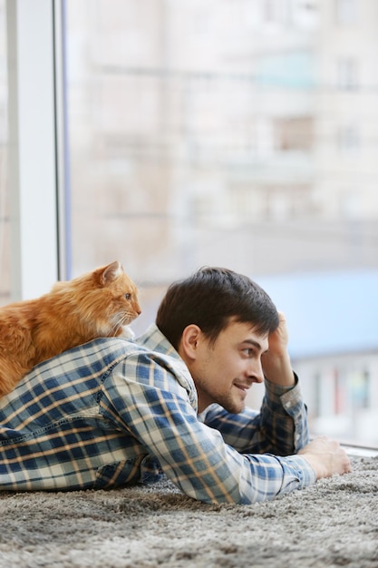 Jonge man met pluizige kat liggend op een tapijt