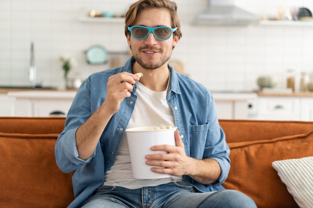 Jonge man met popcorn in handen thuis tv-kijken.