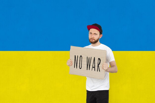 Jonge man met poster met No War-letters geïsoleerd op blauwe en gele achtergrond