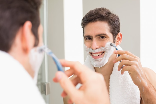 Foto jonge man met reflectie scheren in de badkamer