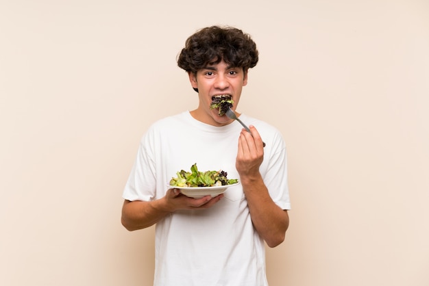 Jonge man met salade over geïsoleerde groene muur
