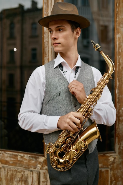 Jonge man met saxofoon staande op balkonterras thuis. Muziek oefenen tijdens weekend vrije tijd