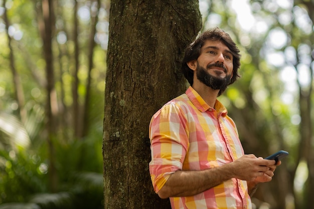 Jonge man met smartphone overdag met een groen park op de achtergrond mobiele telefoon technologie