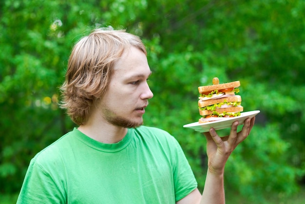 Jonge man met stuk grote worst sandwich op bord Student eet fastfood