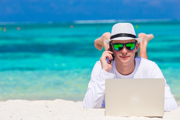 Jonge man met tablet pc en mobiele telefoon op tropisch strand