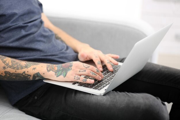 Jonge man met tatoeage met laptop op een bank thuis