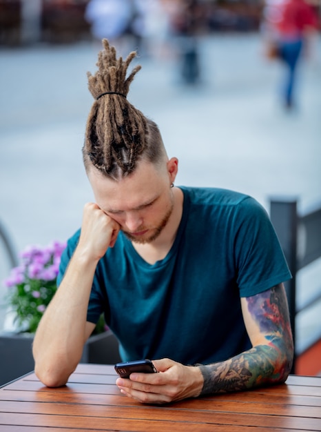 Foto jonge man met telefoon zit aan tafel in een café in de stad