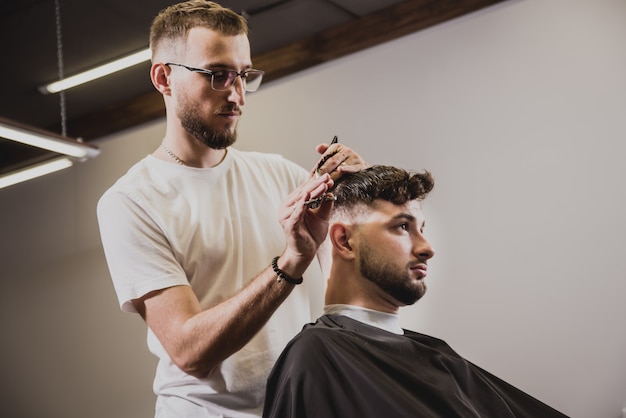 Jonge man met trendy kapsel bij kapper. Kapper doet het kapsel en baard trimmen.