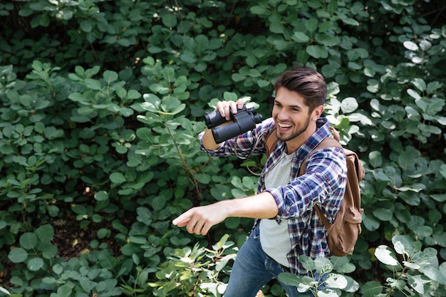 Jonge man met verrekijker in het bos laat ons zien