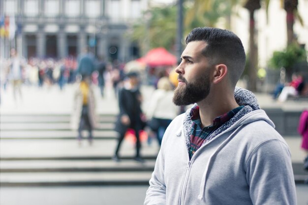 Jonge man met volle baard in profiel op zoek naar iemand op straat in de stad aantrekkelijke hipster