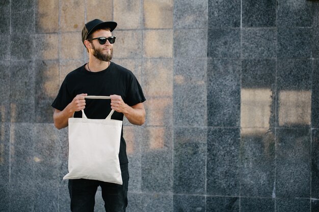 Jonge man met witte eco textielzak tegen de achtergrond van de stedelijke stad. ecologie of milieubescherming concept. witte eco-tas voor mock-up.