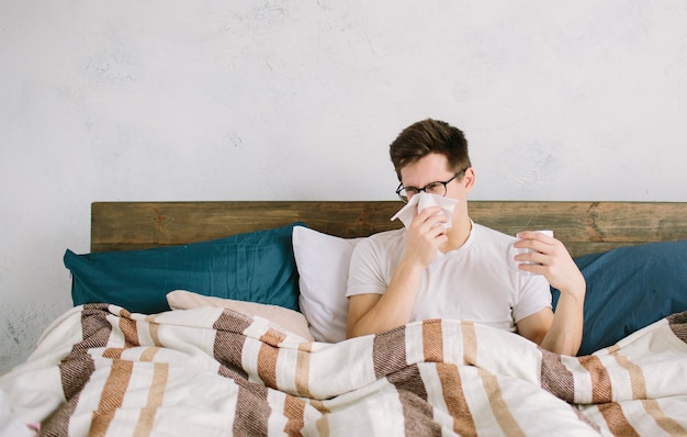 Jonge man met zakdoek. Zieke man op bed heeft een loopneus. man maakt een remedie voor verkoudheid.