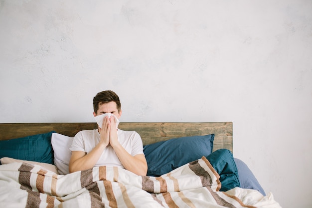 Jonge man met zakdoek. Zieke man op het bed heeft een loopneus. man maakt een remedie tegen verkoudheid