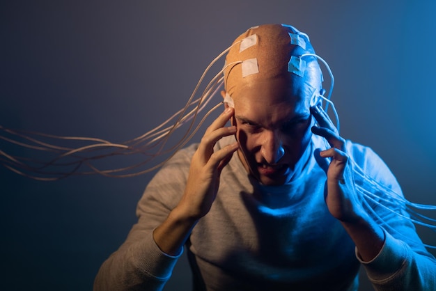 Jonge man met zijn hoofd verstrikt in draden die pijn en lijden ervaart en zijn hoofd elektrisch vasthoudt...