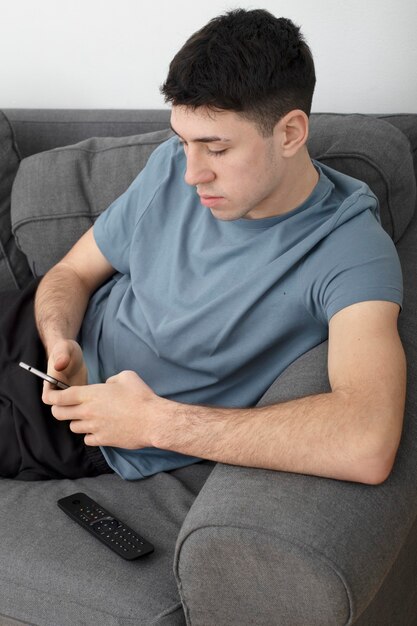 Jonge man op de bank te typen op zijn mobiele telefoon