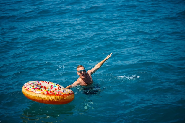 Jonge man op een opblaasbare ring in de zee rusten en zwemmen op een zonnige dag
