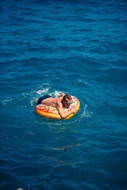 Jonge man op een opblaasbare ring in de zee rusten en zwemmen op een zonnige dag