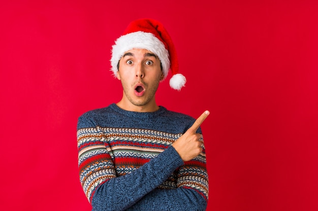 Foto jonge man op kerstdag iets kleins met wijsvingers, glimlachen en zelfverzekerd houden.