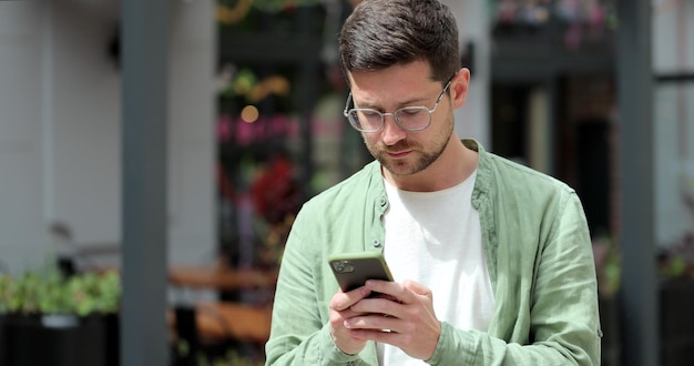 Jonge man op straat in de stad met moderne smartphone in handen Berichten typen op zijn smartphone Online berichten verzenden en surfen op internet Technologie voor levensstijlen