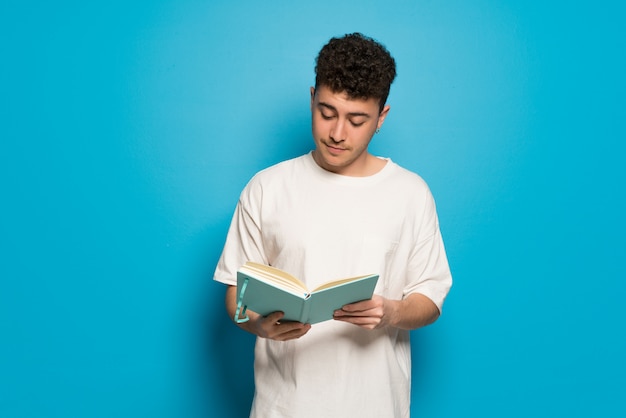 Jonge man over blauw een boek te houden en te genieten van het lezen