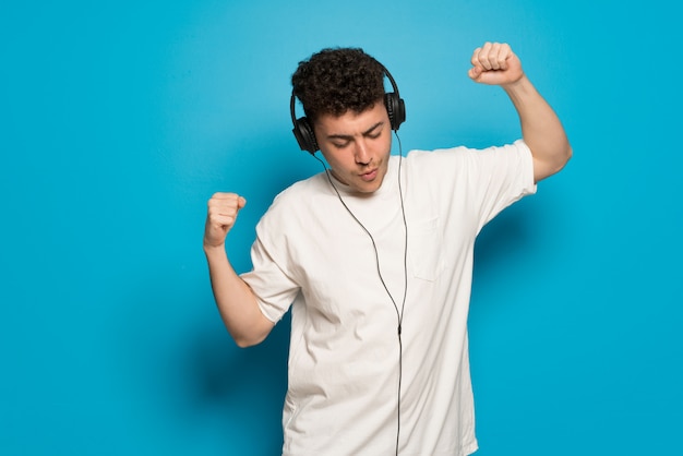 Jonge man over blauw luisteren naar muziek met een koptelefoon en dansen