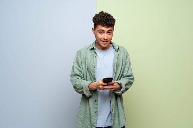 Jonge man over blauwe en groene achtergrond een bericht met de mobiele verzenden