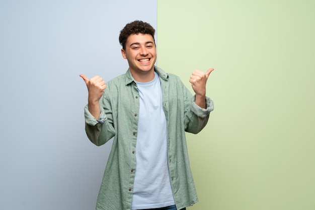 Jonge man over blauwe en groene muur geven een duim omhoog gebaar met beide handen en glimlachen