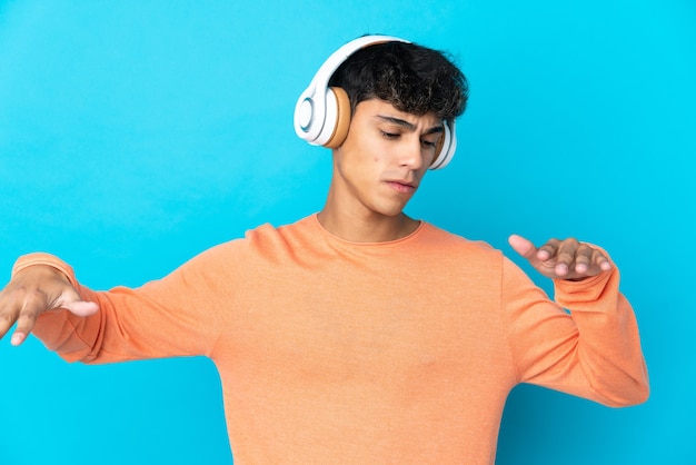 Jonge man over geïsoleerde blauwe achtergrond muziek luisteren en dansen