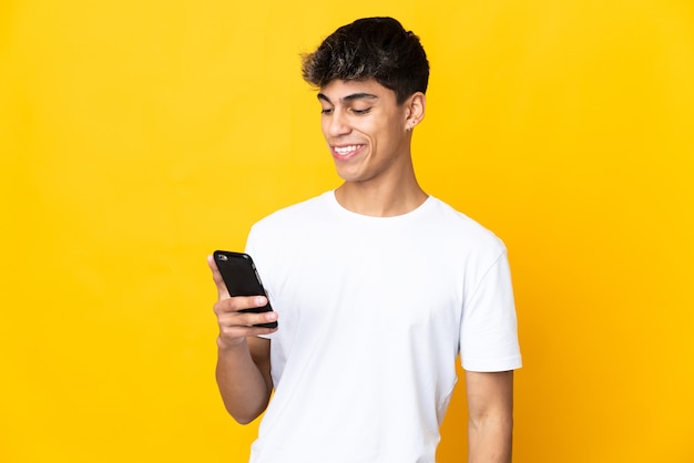Jonge man over geïsoleerde gele achtergrond die een bericht of e-mail met gsm verzendt
