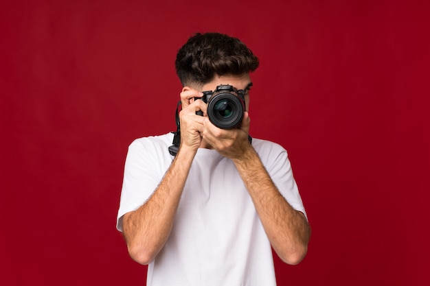 Jonge man over geïsoleerde muur met een professionele camera