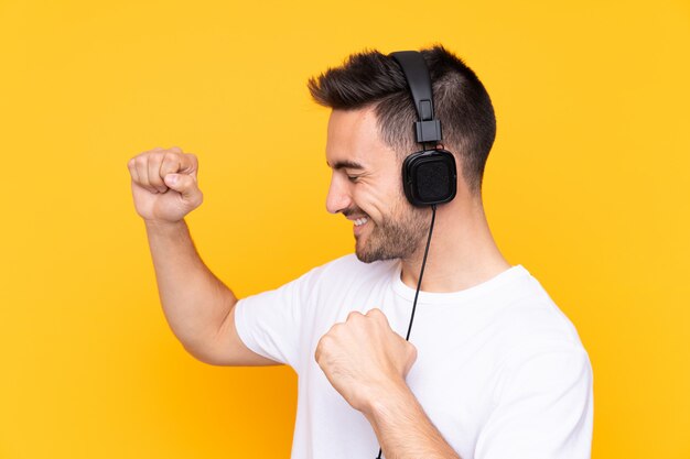 Jonge man over gele muur luisteren muziek en dansen