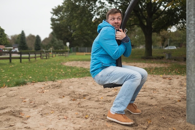 Jonge man plezier op schommel op de speelplaats