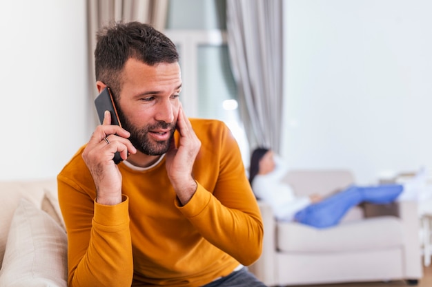 Jonge man praten privé op mobiele telefoon terwijl zijn vrouw tv kijkt achterin.