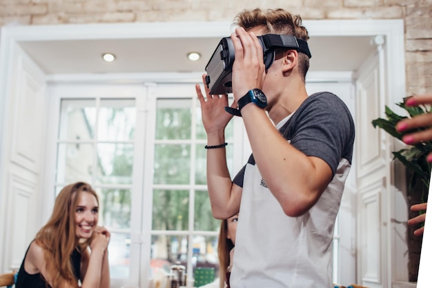 Jonge man probeert een virtual reality-bril terwijl mensen naar hem kijken en lachen in restaurant