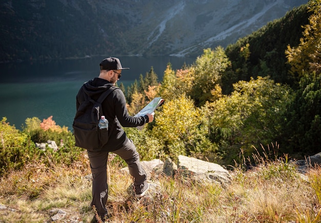 Jonge man reiziger met kaart en rugzak ontspannen buiten met rocky mountains op background