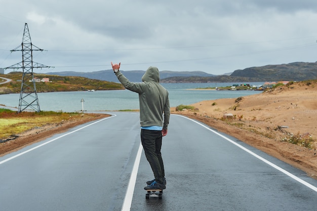 Jonge man rijden op een longboard op lege kronkelende bergweg in de zomer, achteraanzicht.