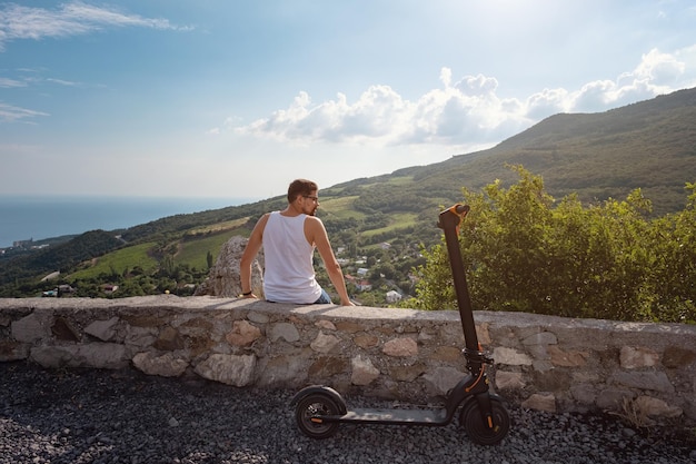 Jonge man rijdt op een elektrische scooter op de bergketen ecologisch transportconcept