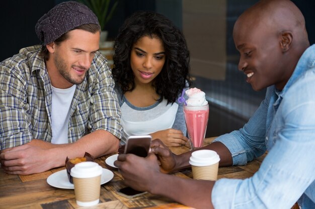 Jonge man slimme telefoon tonen aan vrienden aan tafel in de coffeeshop