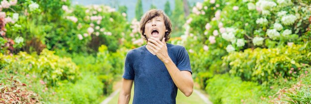 Foto jonge man snuit neus voor bloeiende boom lente allergie concept banner lang formaat