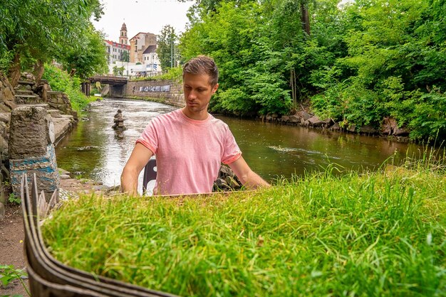 Jonge man spelen verlaten gran piano bedekt met gras, vervallen piano door een rivieroever Vilnia rivier in Uzupis kunstenaarswijk in Vilnius