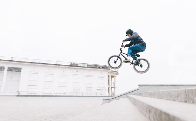 Jonge man springt op de BMX vanaf de trap tegen de achtergrond van een minimalistisch stedelijk landschap