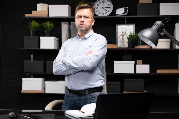 Jonge man staat in de buurt van de computer tafel en vouwde zijn handen op zijn borst