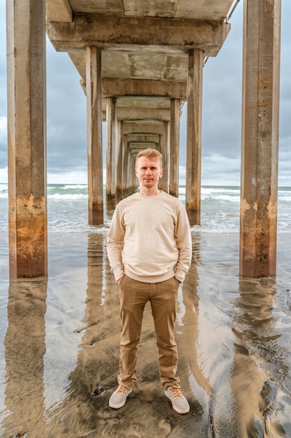 Jonge man staat onder de pier in La Jolla Shores op de bewolkte tijd Symmetrical Pier in San Dieg