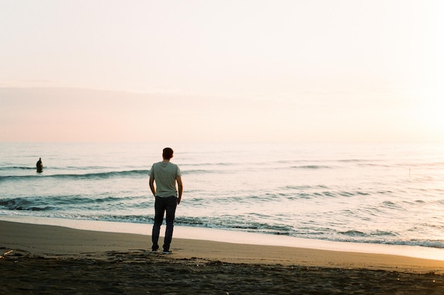 Jonge man staat op het strand en kijkt naar de zonsondergang Achteraanzicht