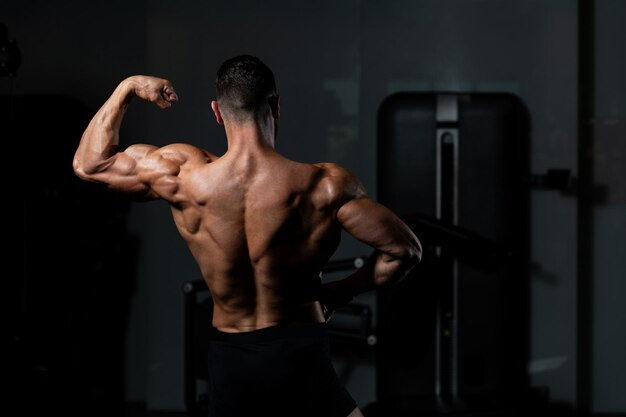 Jonge man staat sterk in de sportschool en buigt spieren Gespierde atletische bodybuilder Fitness Model poseren na oefeningen