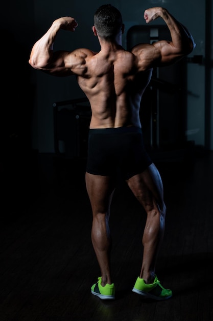 Jonge man staat sterk in de sportschool en buigt spieren Gespierde atletische bodybuilder Fitness Model poseren na oefeningen