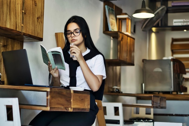 jonge man studeert op zijn laptop, leest een boek en drinkt koffie, blogger, ontwerpstudent, laat