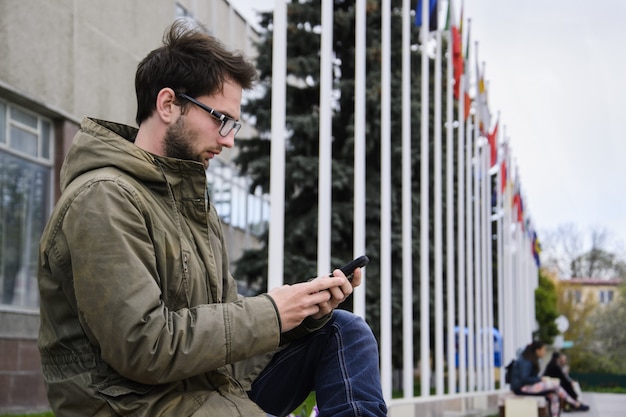 Jonge man texting in een mobiele telefoon zittend op een bankje op het plein