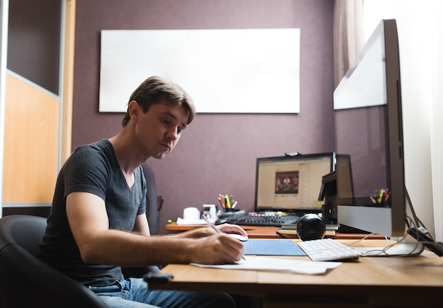 Jonge man thuis met behulp van een computer, freelance ontwikkelaar of ontwerper thuis werken.